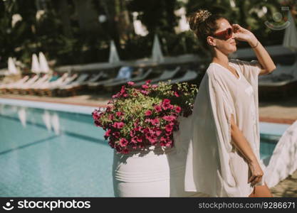 Pretty young woman standing next to the swimming pool and enjoying the sun