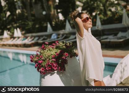 Pretty young woman standing next to the swimming pool and enjoying the sun