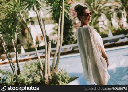 Pretty young woman standing next to the swimming pool and enjoying the sun