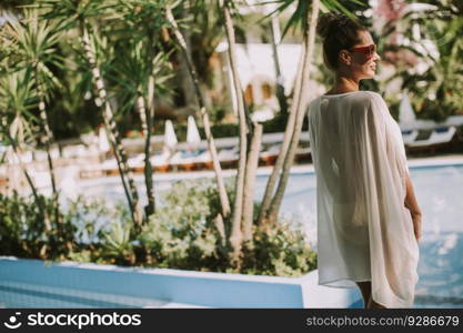 Pretty young woman standing next to the swimming pool and enjoying the sun