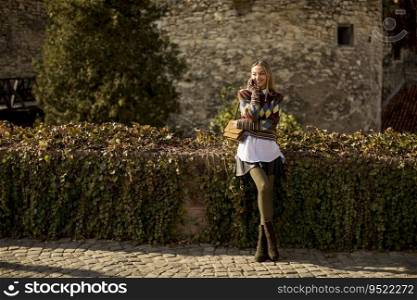 Pretty young woman standing with mobile phone on street at sunny autumn day