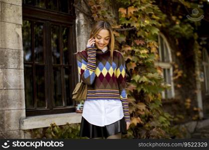 Pretty young woman standing with mobile phone on street at sunny autumn day