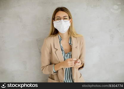 Pretty young woman standning by the grey wall and wearing a respiratory mask from coronavirus disease