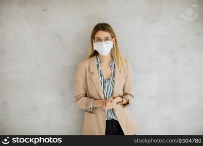 Pretty young woman standning by the grey wall and wearing a respiratory mask from coronavirus disease