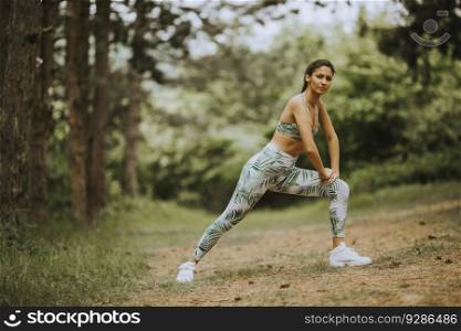 Pretty young woman stretching and breathing fresh air in middle of forest while exercising