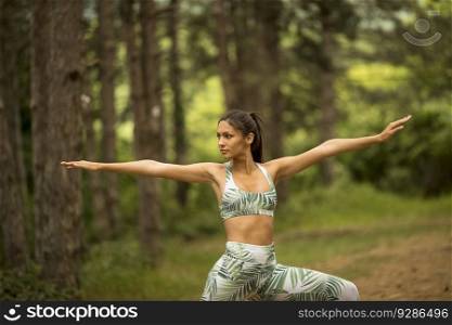 Pretty young woman stretching and breathing fresh air in middle of forest while exercising