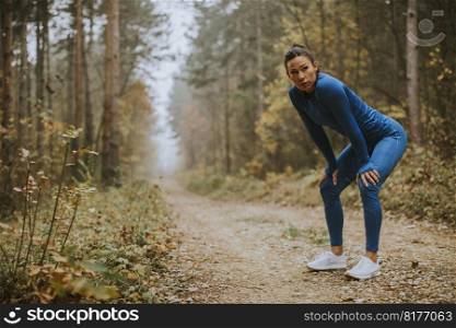 Pretty young woman take a break during outdoor exercise on the forest trail at autumn