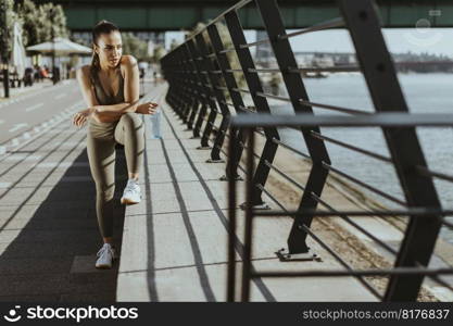 Pretty young woman taking a break during exercise on the river promenade