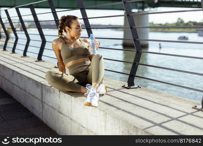 Pretty young woman taking a break during exercise on the river promenade