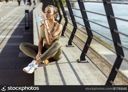 Pretty young woman taking a break during exercise on the river promenade