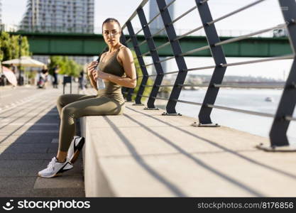 Pretty young woman taking a break during exercise on the river promenade