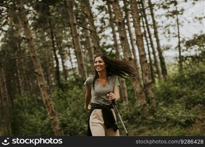 Pretty young woman taking a walk with trekking poles in the forest, carrying a backpack