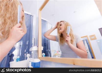 Pretty young woman taking care of haircare, brushing wet blonde hair after taking a shower feeling fresh.. Woman brushing her wet blonde hair