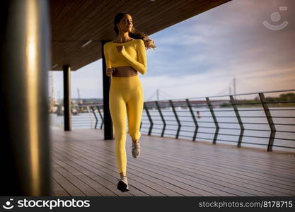 Pretty young woman taking running exercise by the river promenade