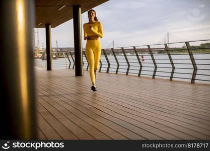 Pretty young woman taking running exercise by the river promenade