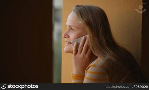 Pretty young woman talking on the phone by the window