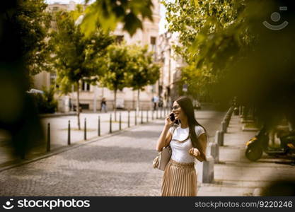 Pretty young woman using a mobi≤pho≠whi≤walking on the street