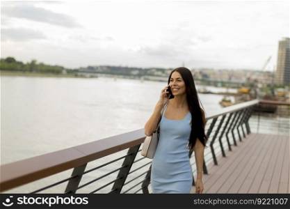 Pretty young woman using a mobile phone while walking on the river promenade