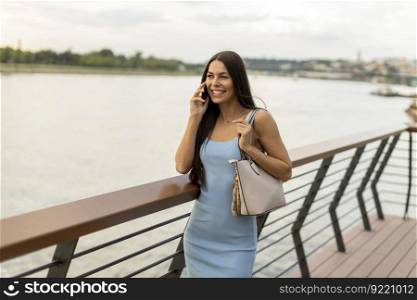 Pretty young woman using a mobile phone while walking on the river promenade