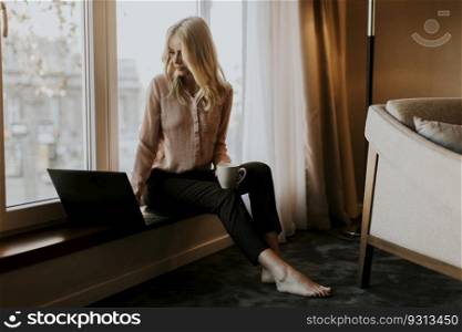 Pretty young woman using laptop and sitting by window