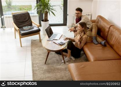 Pretty young woman using laptop and young man using digital tablet while sitting on sofa at home