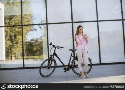 Pretty young woman using mobile phone by modern city electric e-bike as clean sustainable urban transportation