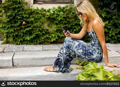 Pretty young woman using mobile phone by old house with ivy