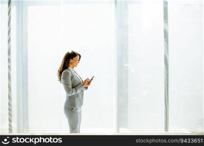 Pretty young woman using mobile phone by the office window