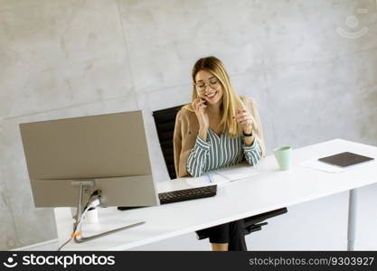 Pretty young woman using mobile phone while sitting by the desk in the office