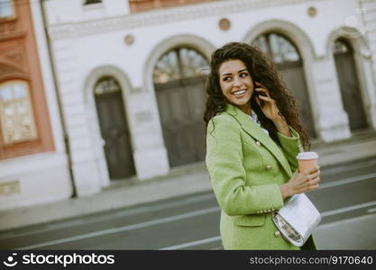 Pretty young woman using smartphone on the street and holding takeaway coffee