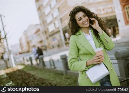 Pretty young woman using smartphone on the street and holding takeaway coffee