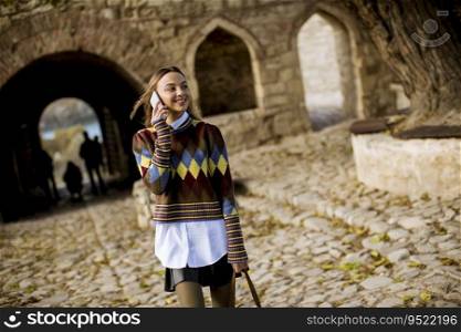 Pretty young woman walking in the autumn park and using a mobile phone