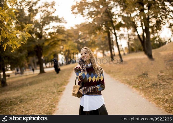 Pretty young woman walking in the autumn park and using a mobile phone