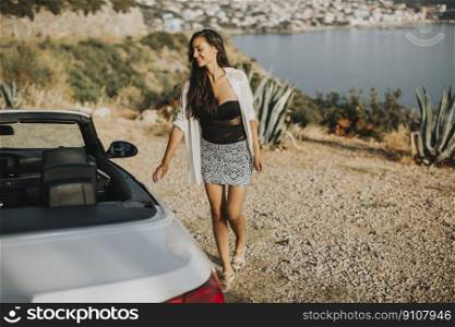 Pretty young woman walking to cabriolet car at seaside
