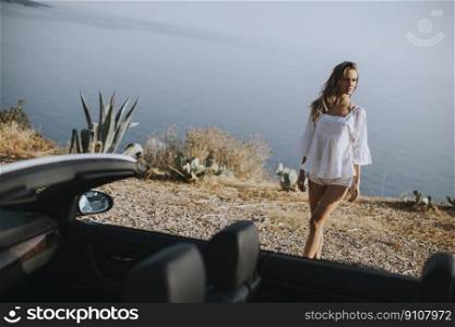Pretty young woman walking to cabriolet car at seaside