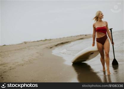 Pretty young woman walking with paddle board on the beach on a summer day