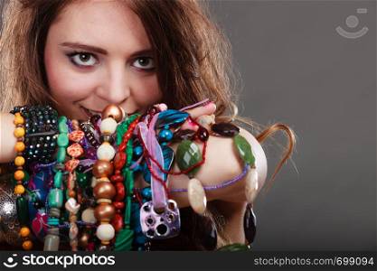 Pretty young woman wearing bracelets holding many plentiful of precious jewelry necklaces beads. Portrait of gorgeous fashion girl in studio on gray.. Pretty woman with jewelry necklaces ring bracelets