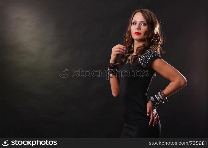 Pretty young woman wearing multiple bracelets jewellery necklace in black elegant evening dress on dark