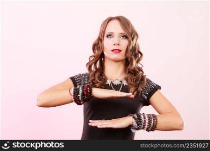 Pretty young woman wearing multiple bracelets jewellery necklace in black elegant evening dress on pink