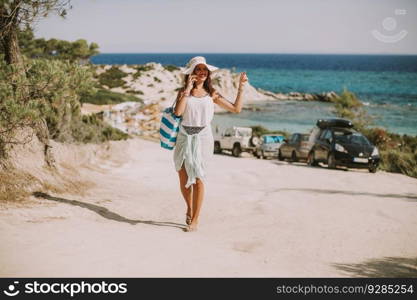 Pretty young woman with a bag using mobile phone on the beach at sunny summer day