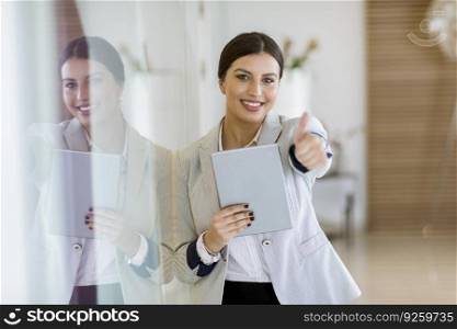 Pretty young woman with a digital tablet in the modern office showing thumb up