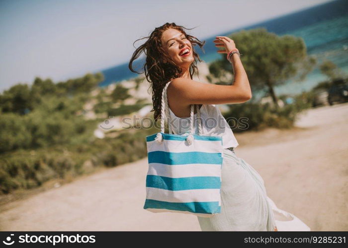 Pretty young woman with bag on the beach on a hot summer day