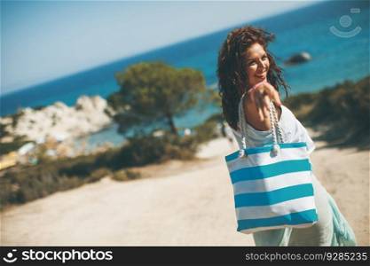 Pretty young woman with bag on the beach on a hot summer day