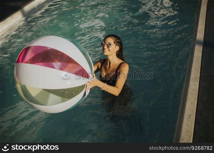 Pretty young woman with ball in the swimming pool at sunny day