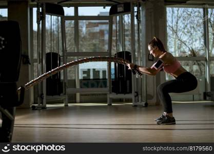 Pretty young woman with battle ropes exercise in the fitness gym