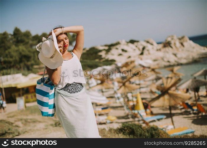 Pretty young woman with beach bag talking on mobile phone by the sea at summer