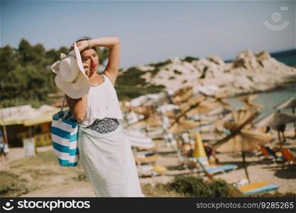 Pretty young woman with beach bag talking on mobile phone by the sea at summer