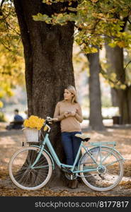 Pretty young woman with bicycle using smartphone in autumn park