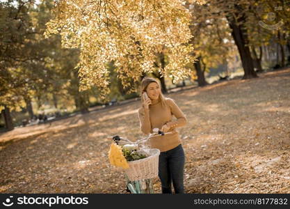 Pretty young woman with bicycle using smartphone in autumn park