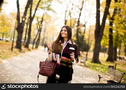 Pretty young woman with coffee cup in the autumn park